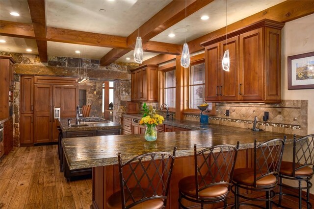 kitchen with a kitchen breakfast bar, kitchen peninsula, decorative light fixtures, beam ceiling, and wood-type flooring