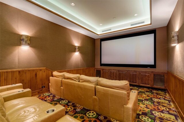 home theater with a tray ceiling and wood walls