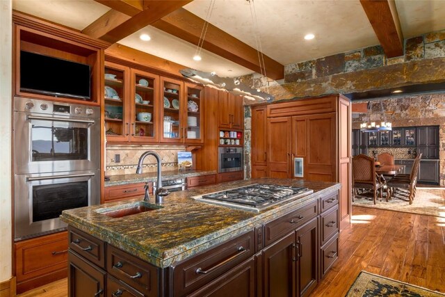 kitchen featuring appliances with stainless steel finishes, sink, beam ceiling, light hardwood / wood-style floors, and an island with sink