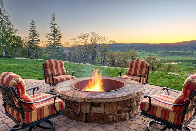 patio terrace at dusk with a lawn, a mountain view, and an outdoor fire pit