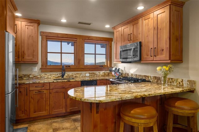 kitchen featuring kitchen peninsula, appliances with stainless steel finishes, light stone countertops, a kitchen breakfast bar, and sink