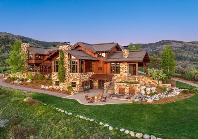 back of property featuring a mountain view, a patio, a fire pit, and a lawn