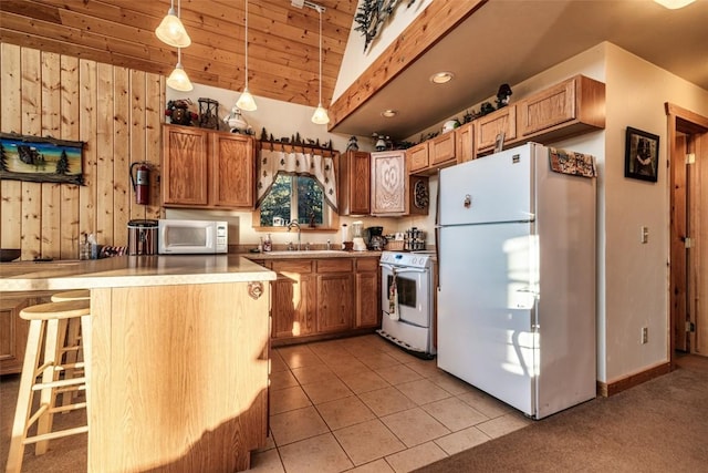 kitchen featuring a peninsula, a kitchen breakfast bar, light tile patterned flooring, white appliances, and a sink