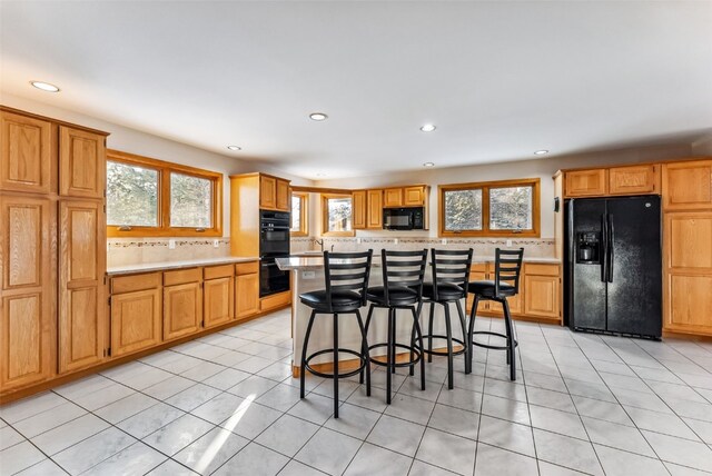 kitchen featuring light tile patterned flooring, a center island, a wealth of natural light, and black appliances