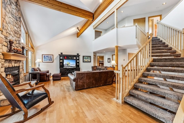 living room with beam ceiling, high vaulted ceiling, a stone fireplace, and light hardwood / wood-style floors