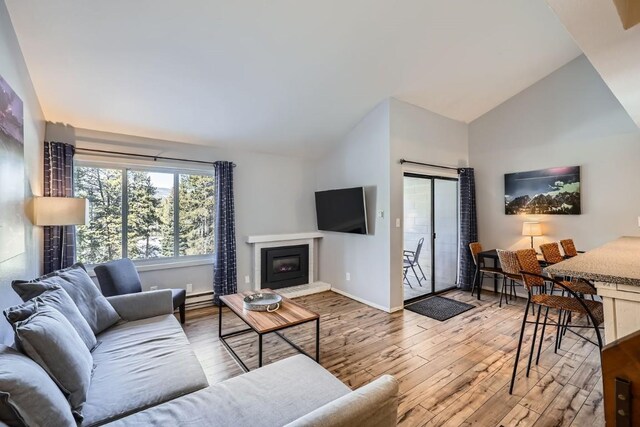 living room with a baseboard heating unit, light hardwood / wood-style flooring, and high vaulted ceiling