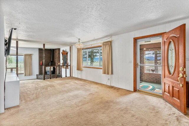 unfurnished living room with a wealth of natural light, carpet, a textured ceiling, and an inviting chandelier