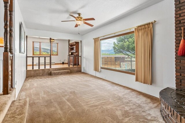 unfurnished living room featuring carpet floors, ceiling fan, and a baseboard heating unit