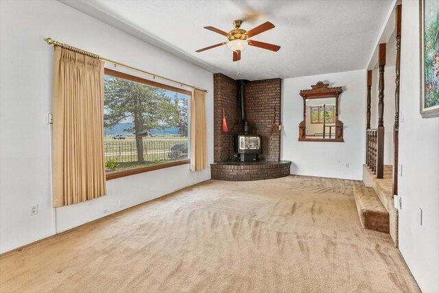 unfurnished living room with carpet, a wood stove, and ceiling fan