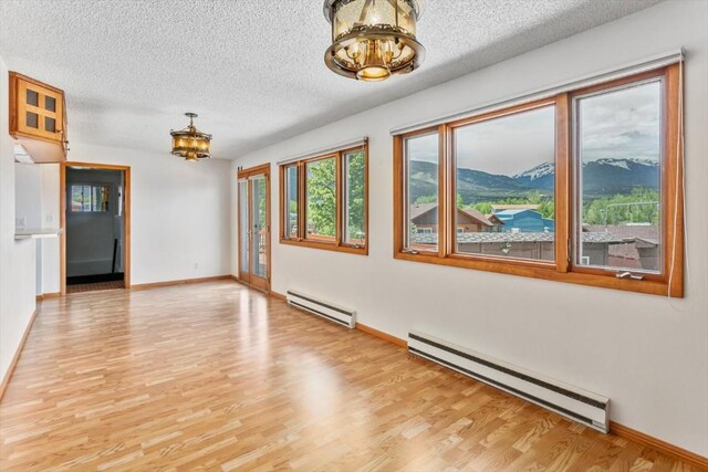 unfurnished room with a mountain view, a textured ceiling, light wood-type flooring, and a baseboard radiator