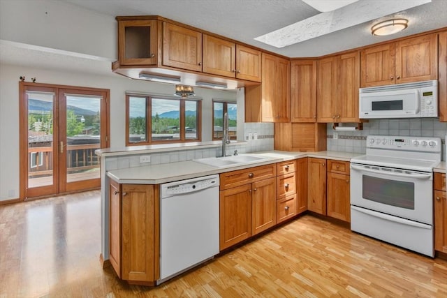 kitchen featuring white appliances, backsplash, sink, a skylight, and light wood-type flooring