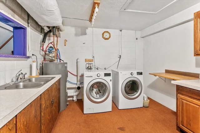 clothes washing area with cabinets, a textured ceiling, gas water heater, washer and clothes dryer, and sink