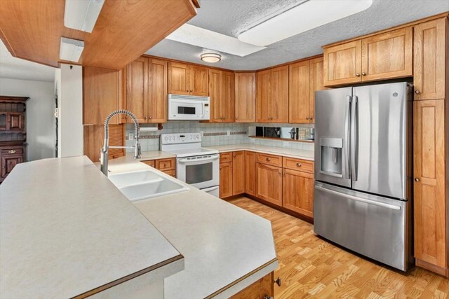 kitchen with tasteful backsplash, white appliances, sink, and light hardwood / wood-style flooring