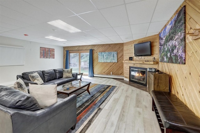 living room featuring a paneled ceiling, wood walls, light hardwood / wood-style floors, and a baseboard heating unit