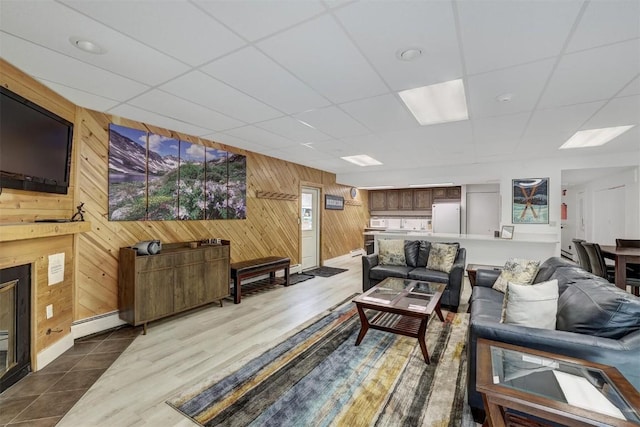 living room with a paneled ceiling, wooden walls, and a baseboard heating unit