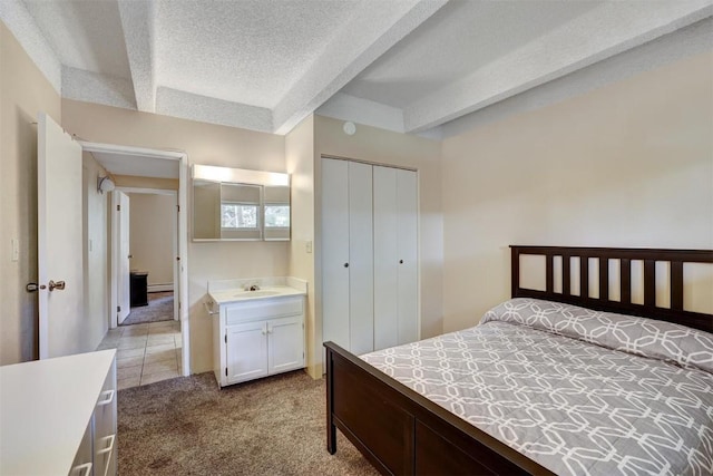 bedroom with a textured ceiling, light colored carpet, sink, beam ceiling, and a closet