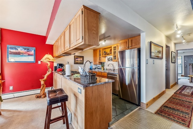 kitchen featuring dark stone counters, a baseboard radiator, a kitchen bar, kitchen peninsula, and stainless steel appliances