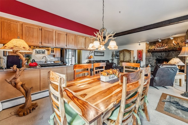 carpeted dining space with rail lighting, a baseboard radiator, beamed ceiling, a notable chandelier, and a fireplace