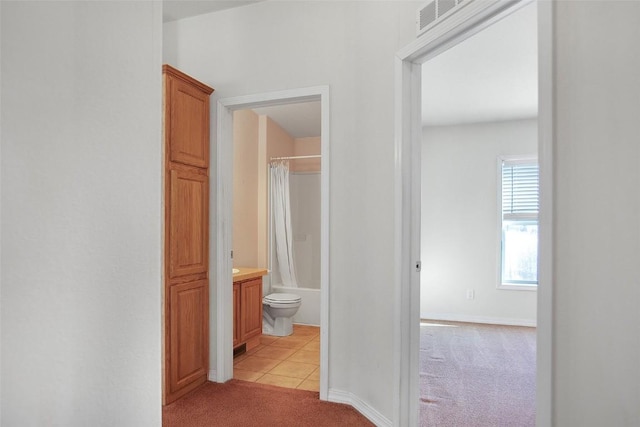 hallway with light carpet, visible vents, baseboards, and light tile patterned floors