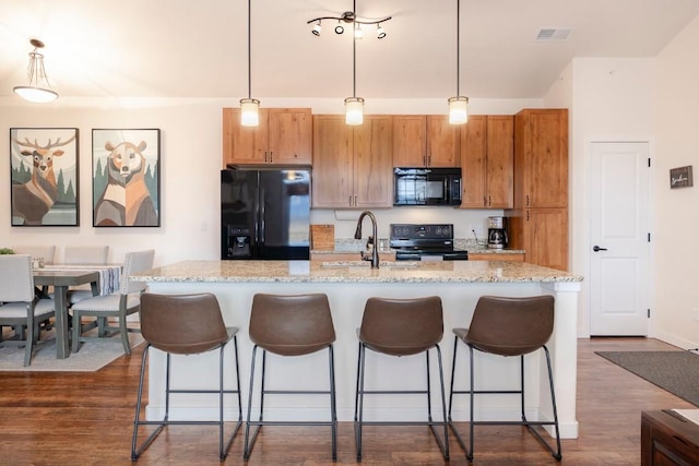 kitchen featuring decorative light fixtures, a kitchen island with sink, and black appliances