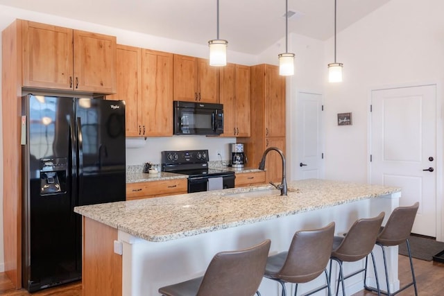 kitchen featuring a center island with sink, hanging light fixtures, and black appliances