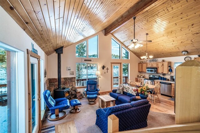 living room with a wood stove, beamed ceiling, high vaulted ceiling, light colored carpet, and ceiling fan with notable chandelier