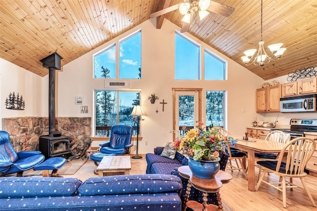 living room featuring ceiling fan with notable chandelier, light wood-type flooring, high vaulted ceiling, and a wood stove