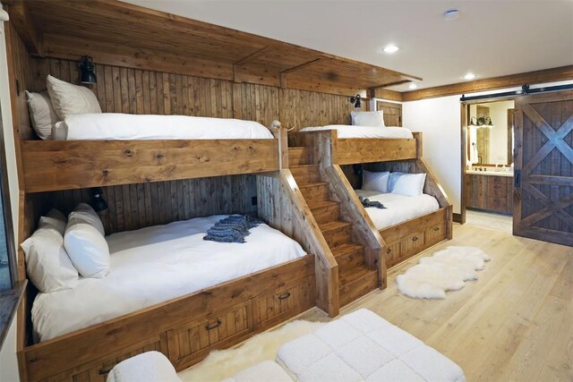 bedroom featuring connected bathroom, light hardwood / wood-style floors, a barn door, and wooden walls