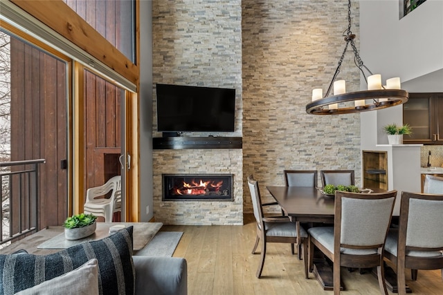 dining area with a stone fireplace, a towering ceiling, a chandelier, and light wood-type flooring