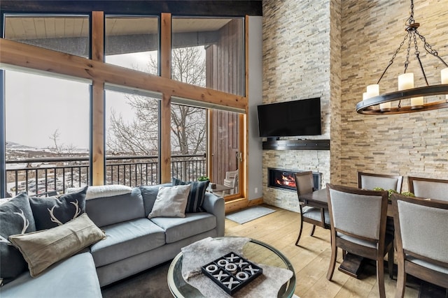 living room featuring a stone fireplace, high vaulted ceiling, a notable chandelier, and light hardwood / wood-style floors