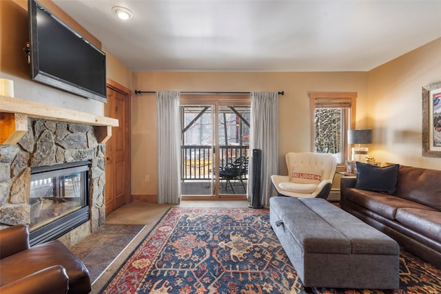 carpeted living area featuring a stone fireplace and baseboards