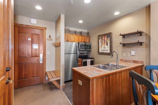 kitchen with a peninsula, a sink, appliances with stainless steel finishes, and tile counters