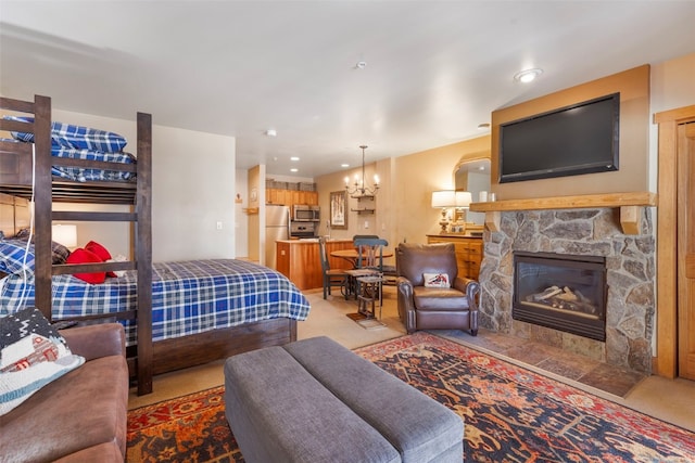 bedroom featuring an inviting chandelier, a fireplace, freestanding refrigerator, and light colored carpet