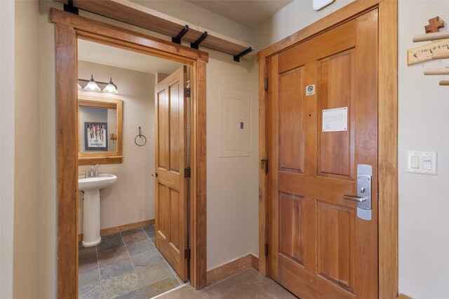 interior space featuring stone finish floor, a sink, electric panel, and baseboards