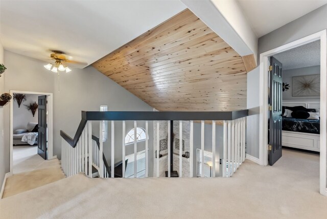 corridor featuring baseboards, lofted ceiling, wooden ceiling, carpet flooring, and an upstairs landing