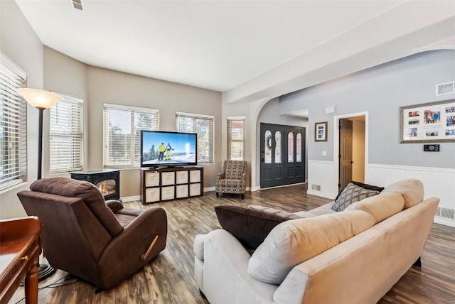 living area featuring arched walkways, a wood stove, dark wood finished floors, and visible vents