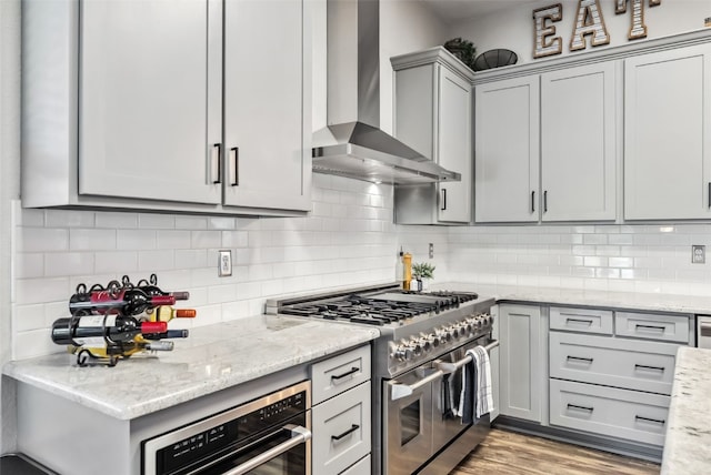 kitchen featuring decorative backsplash, wall chimney exhaust hood, light wood-style flooring, gray cabinets, and stainless steel appliances