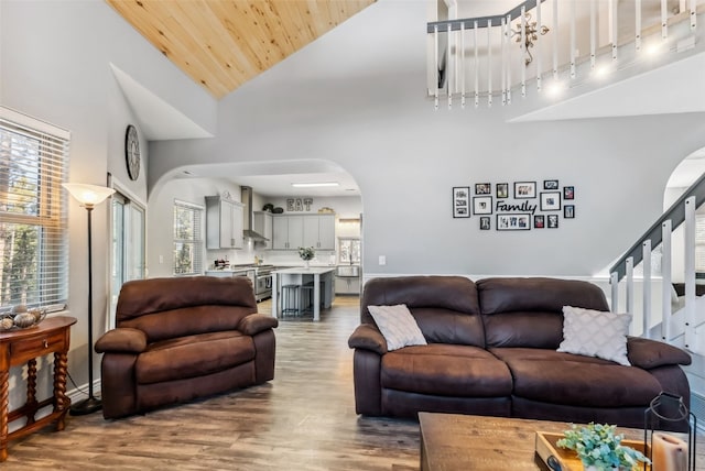 living room with arched walkways, wood ceiling, wood finished floors, high vaulted ceiling, and stairs