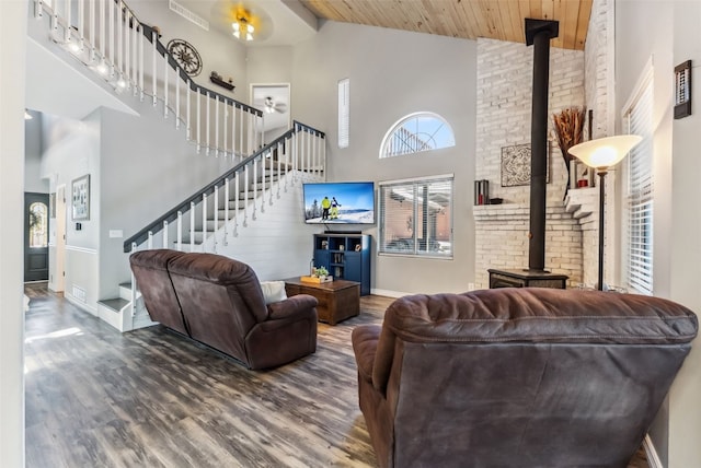 living room featuring visible vents, stairway, a wood stove, wood finished floors, and high vaulted ceiling