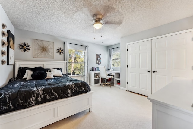 bedroom with a textured ceiling, ceiling fan, a closet, and light colored carpet