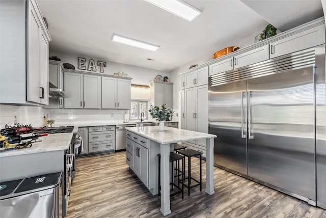 kitchen featuring extractor fan, gray cabinetry, a breakfast bar, wood finished floors, and high quality appliances