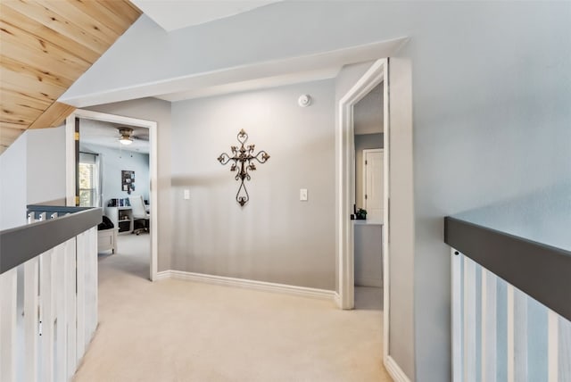 hall featuring wooden ceiling, light colored carpet, an upstairs landing, baseboards, and vaulted ceiling