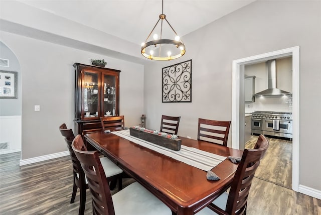 dining space with arched walkways, baseboards, wood finished floors, and an inviting chandelier