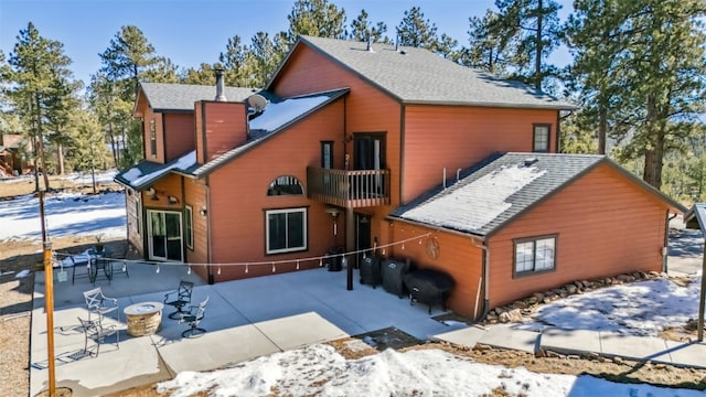 snow covered property featuring a shingled roof, a patio, and a balcony