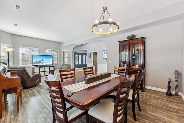 dining space with baseboards, visible vents, arched walkways, wood finished floors, and a chandelier