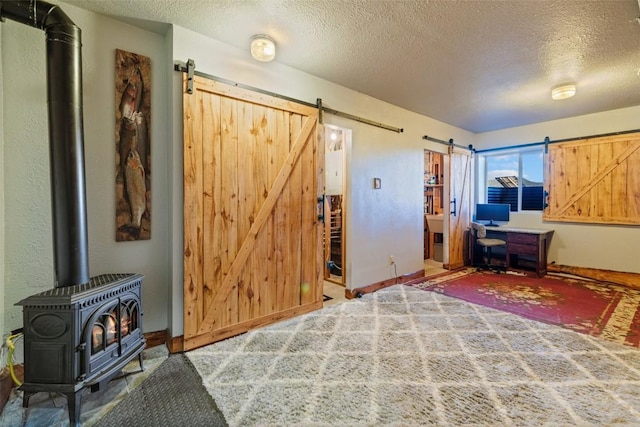 bedroom featuring a wood stove, carpet, a textured ceiling, and a barn door