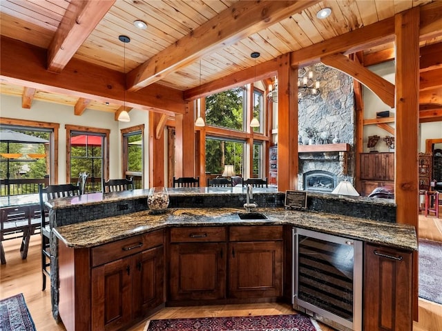 kitchen with pendant lighting, a stone fireplace, wine cooler, dark stone countertops, and light hardwood / wood-style floors