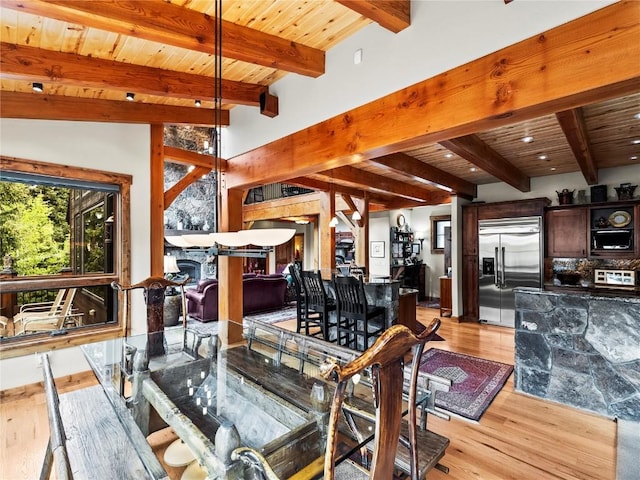 dining space featuring a stone fireplace, lofted ceiling with beams, wooden ceiling, and light hardwood / wood-style floors