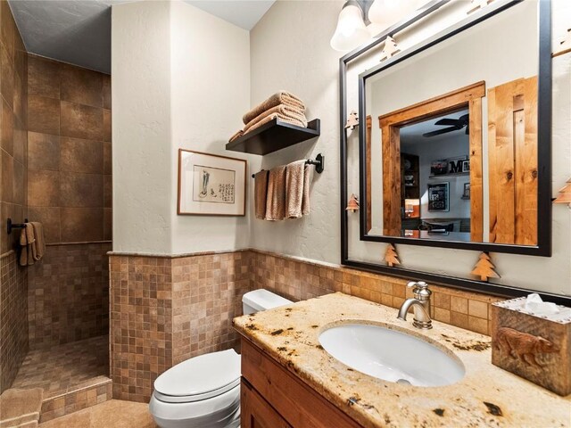 bathroom with a tile shower, vanity, tile walls, and toilet