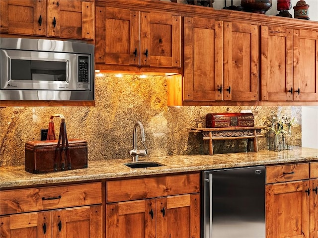 kitchen with decorative backsplash, refrigerator, light stone counters, sink, and stainless steel microwave